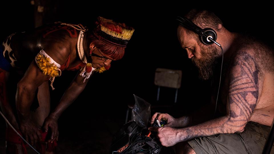 Man in tribal dress leans over music recording equipment